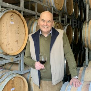 a man standing among wine barrels holding a glass of red wine